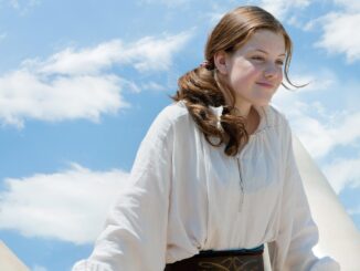 Georgie Henley is playing lucy. She is looking over the side of the Dawn Treader with a partially cloudy blue sky in the background.