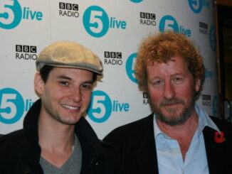 Ben Barnes stands on the left wearing a white hat while Sebastian Faulkes stands to the right. In the background is a white backdrop with the BBC Radio 5 Live logo tiled across the background.