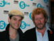 Ben Barnes stands on the left wearing a white hat while Sebastian Faulkes stands to the right. In the background is a white backdrop with the BBC Radio 5 Live logo tiled across the background.