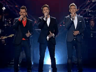 The three member boy band E.M.D. stands on a stage sining "There's a Place for Us" from the Voyage of the Dawn Treader soundtrack