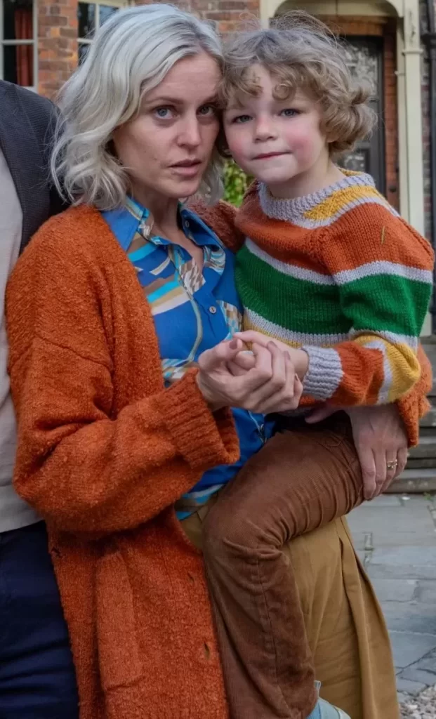 Denise Gough, with a worried expression, holds a young, curly-haired Beatrice Campbell. They stand outside a brick house in a scene from "The Stolen Girl."